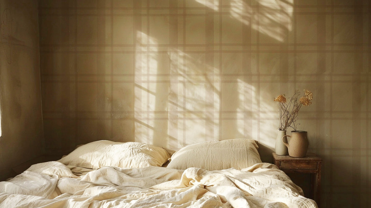 Neutral plaid wallpaper featuring soft beige and blush pink lines forming a classic tartan pattern on a warm cream background, styled in a bedroom