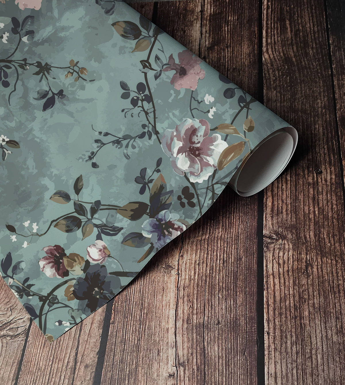 Vintage floral wallpaper with soft pink, cream and purple flowers, dark trailing branches and muted foliage on a dusty sage green background up close.