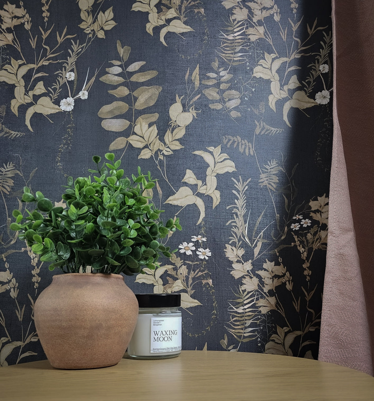 Dark floral wallpaper with vintage botanical leaves, delicate white wildflowers and warm brown foliage on a deep navy blue background on wall.