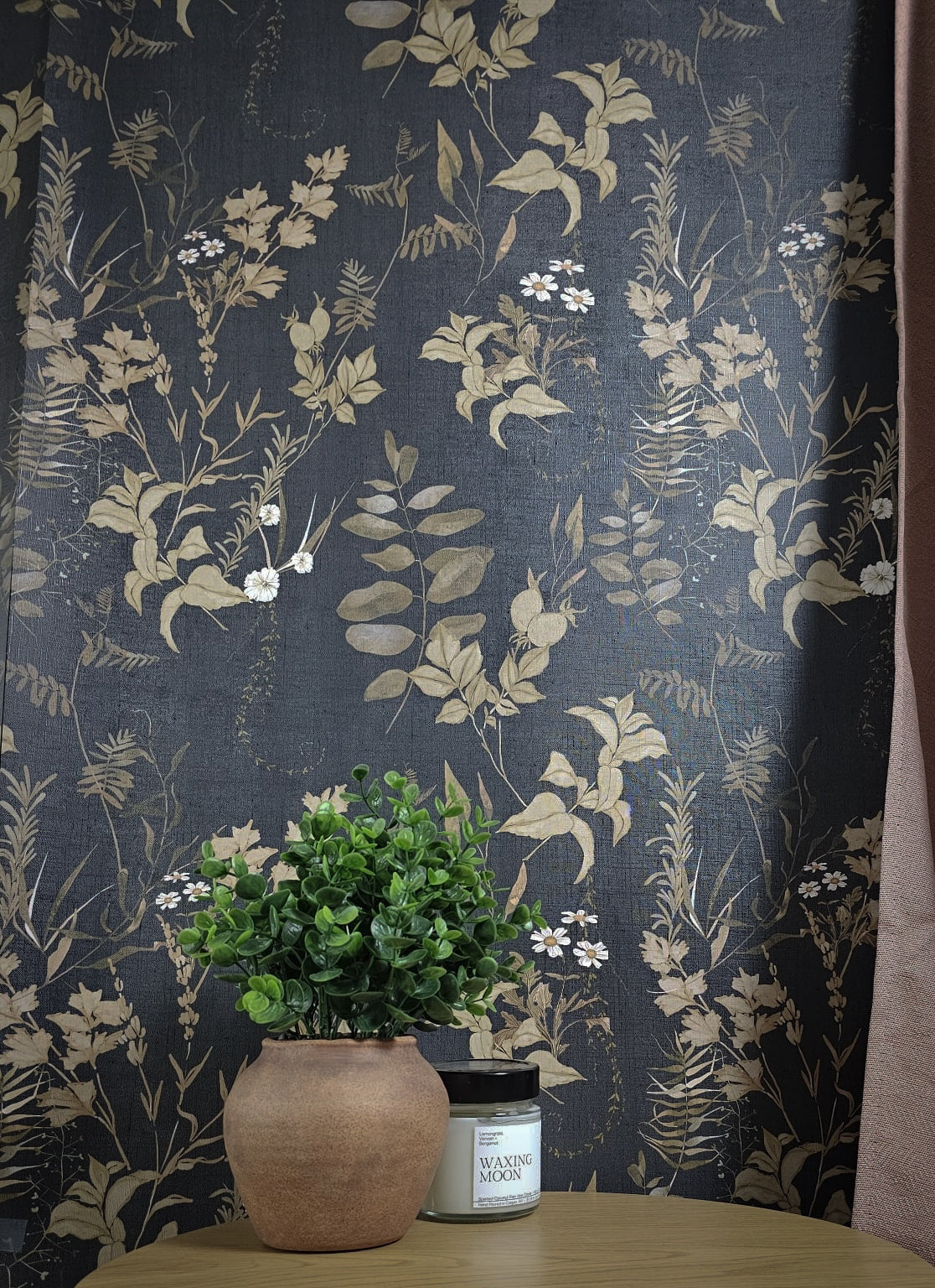 Dark floral wallpaper with vintage botanical leaves, delicate white wildflowers and warm brown foliage on a deep navy blue background on wall.
