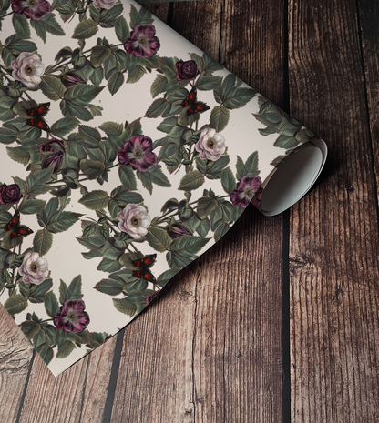 Vampire butterfly wallpaper with moody black and burgundy butterflies among vintage-style roses and green foliage on a soft blush background up close