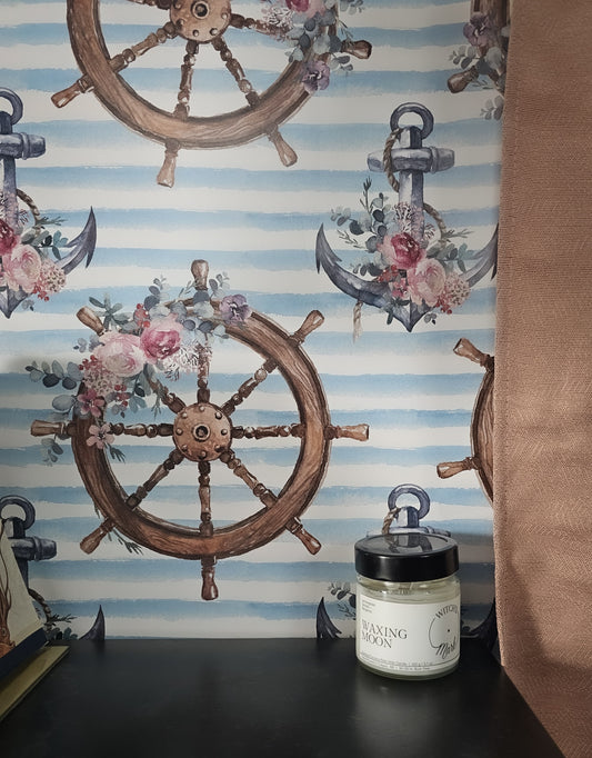 Nautical coastal wallpaper featuring watercolor ship wheels and anchors adorned with pink floral bouquets on soft blue and white striped background up close