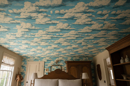 A bedroom interior featuring a ceiling and walls covered in blue sky wallpaper with white clouds, with a bed, wooden headboard, lamps, and shelving visible.