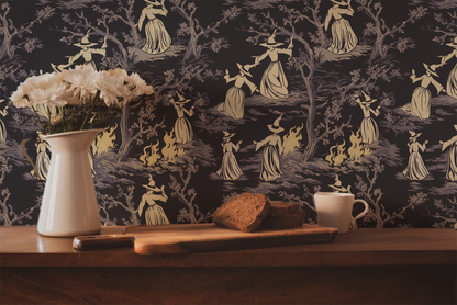 Moody peel-and-stick wallpaper sample featuring a witchy toile pattern with cream-cloaked figures, twisted gray trees, and glowing bonfire details on a deep charcoal background.