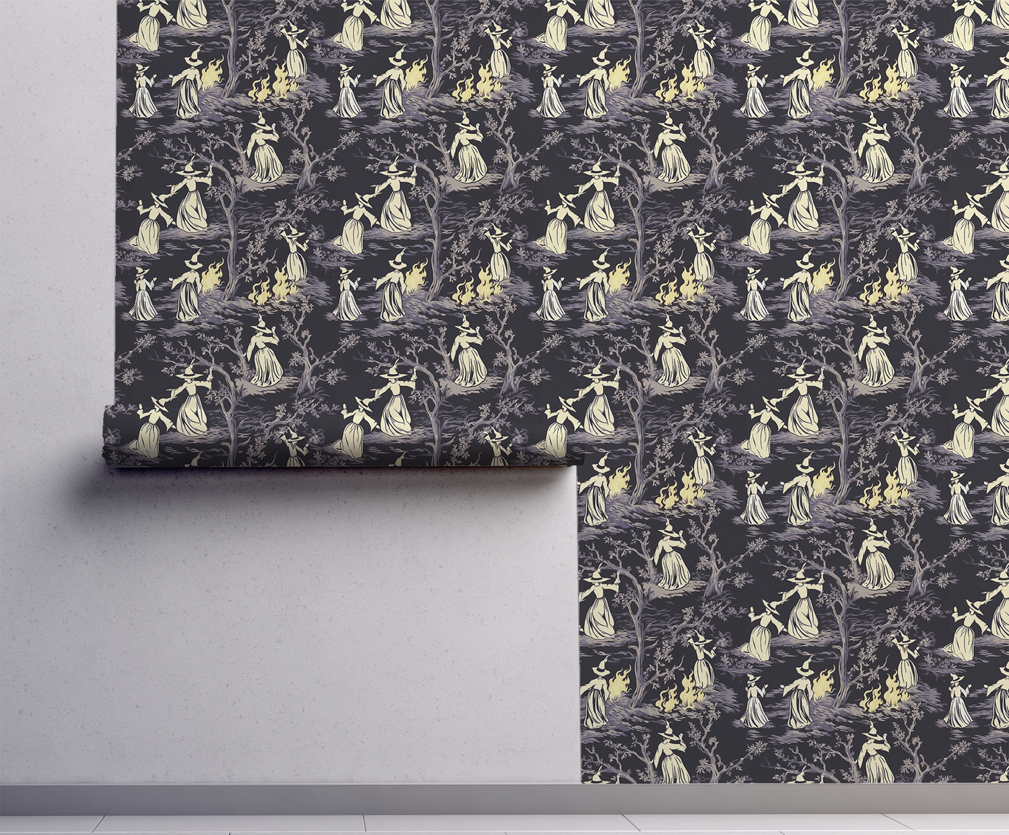 Moody peel-and-stick wallpaper sample featuring a witchy toile pattern with cream-cloaked figures, twisted gray trees, and glowing bonfire details on a deep charcoal background on wall