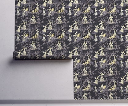 Moody peel-and-stick wallpaper sample featuring a witchy toile pattern with cream-cloaked figures, twisted gray trees, and glowing bonfire details on a deep charcoal background on wall