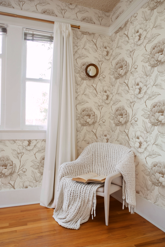 Cozy corner with a chair draped with a blanket, book, and decorative wall clock in a room with floral wallpaper.