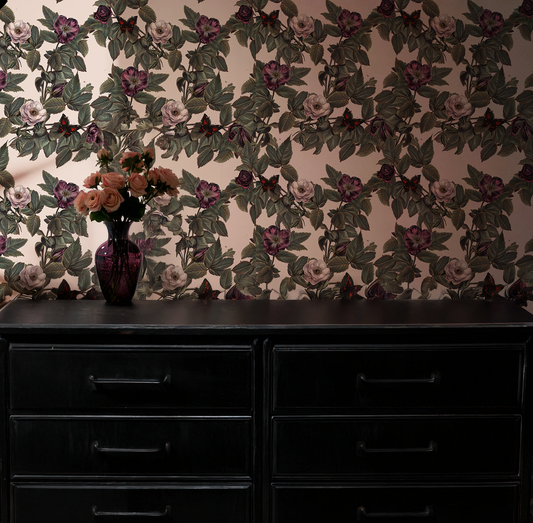 Vampire butterfly wallpaper with moody black and burgundy butterflies among vintage-style roses and green foliage on a soft blush background on wall