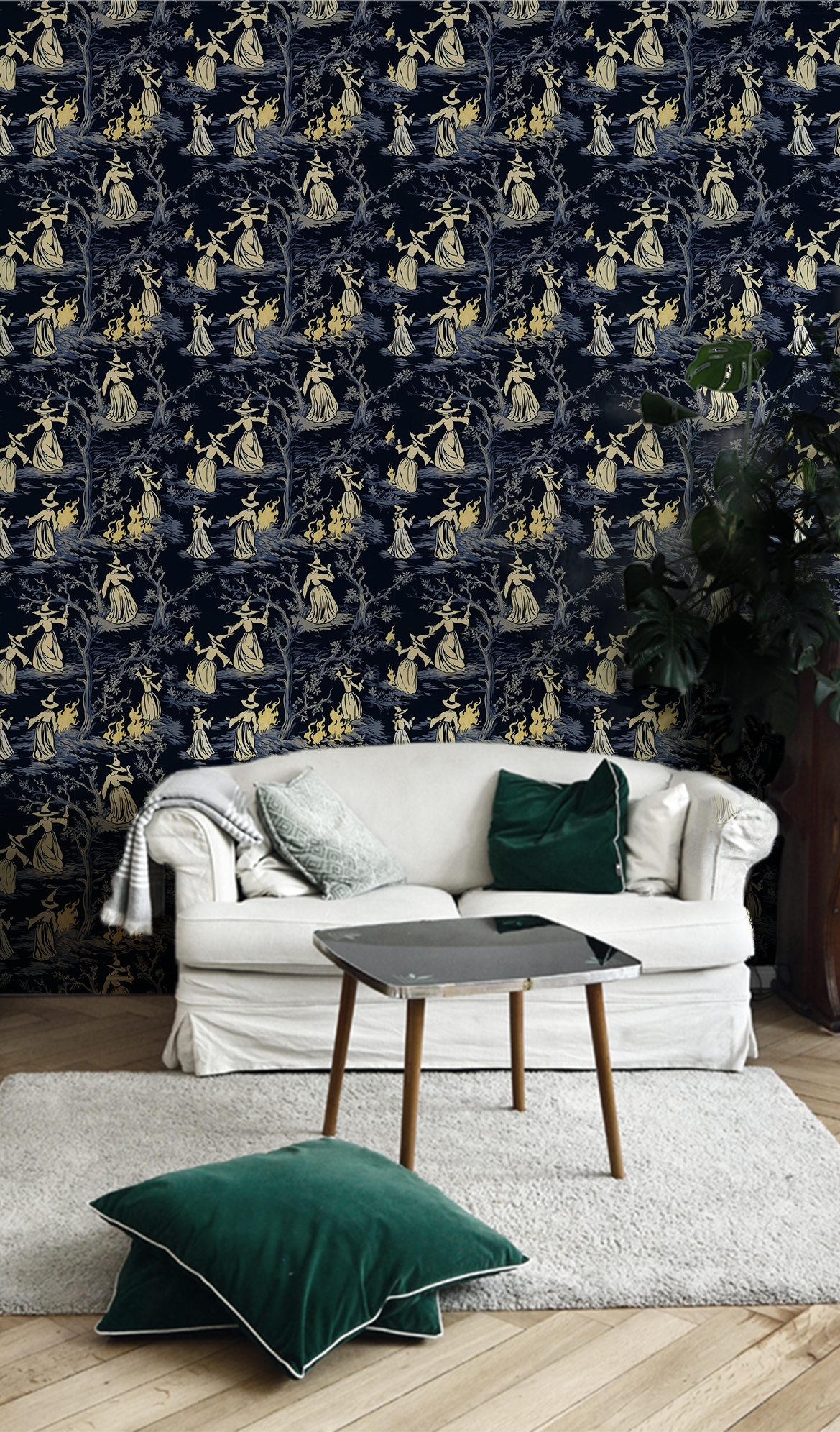 Moody peel-and-stick wallpaper sample featuring a witchy toile pattern with cream-cloaked figures, twisted gray trees, and glowing bonfire details on a deep charcoal background in room