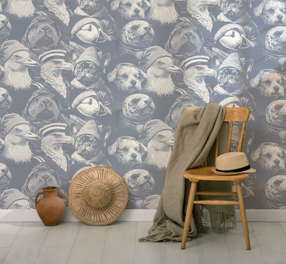Blue peel-and-stick wallpaper sample featuring detailed illustrated animal portraits, including puffins, eagles, pugs, ducks, and sea otters wearing knit hats and sailor caps in a whimsical nautical style  with chair and hat