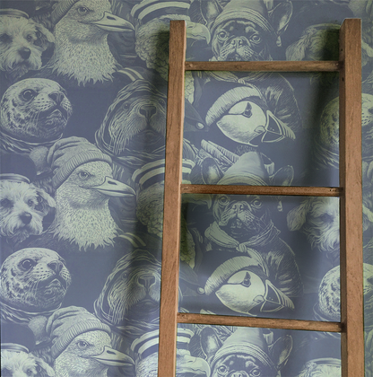 Blue peel-and-stick wallpaper sample featuring detailed illustrated animal portraits, including puffins, eagles, pugs, ducks, and sea otters wearing knit hats and sailor caps in a whimsical nautical style displayed