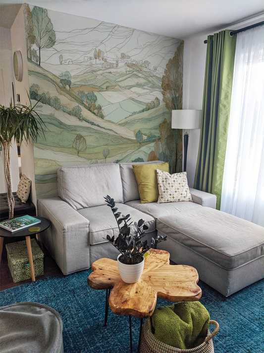 Sage green countryside landscape wall mural with rolling hills behind a living room sofa